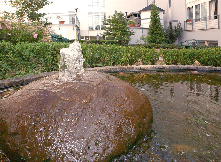 Garten im Gemeinschaftsbereich mit einem großen Stein als Springbrunnen